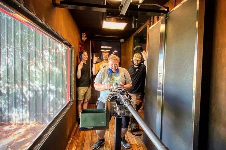 Four people with ear protection around a large mounted machine gun indoors.