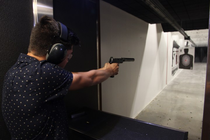 Person wearing earmuffs aiming a handgun at a shooting range target.