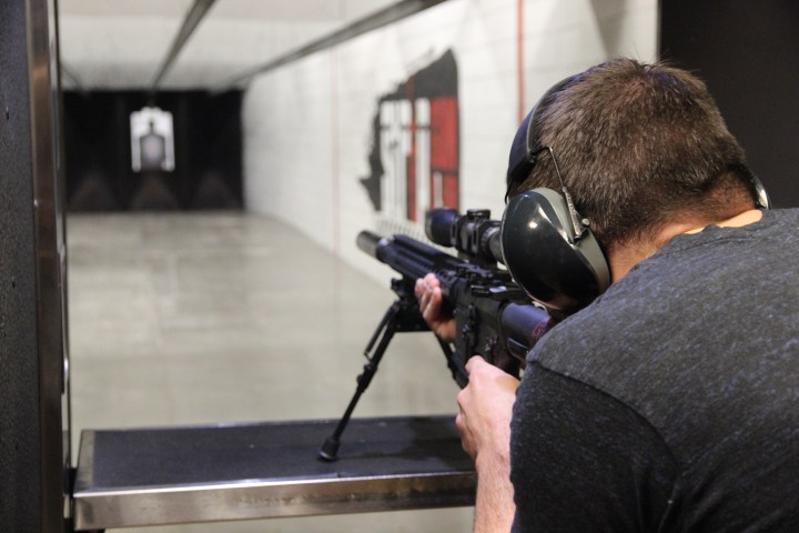 Person aiming a rifle in an indoor shooting range.