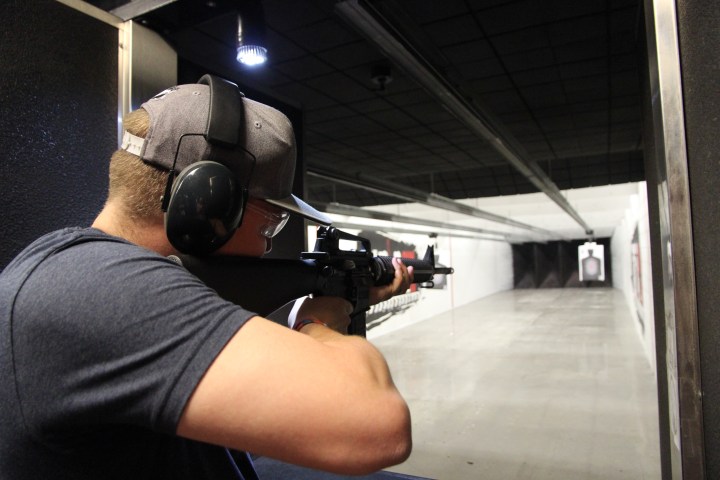Person aiming a rifle at a target in an indoor shooting range.