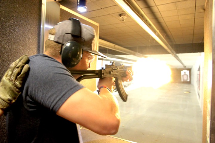Person wearing ear protection firing rifle at indoor shooting range.