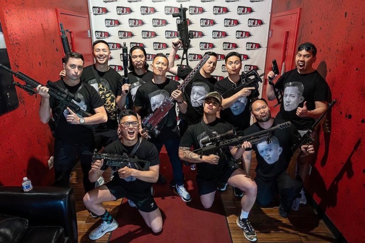 Group of people in black shirts posing with toy guns in a red room.