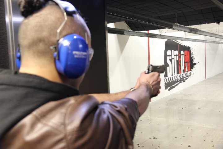 Person wearing earmuffs aiming a handgun at indoor shooting range target.