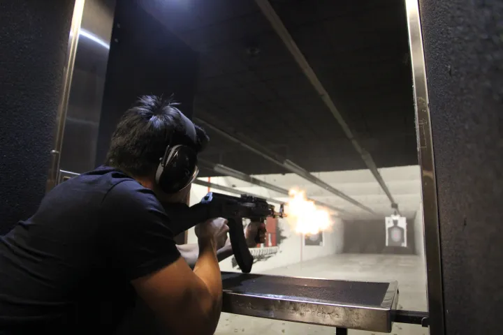 Person firing a rifle at an indoor shooting range, with visible muzzle flash.