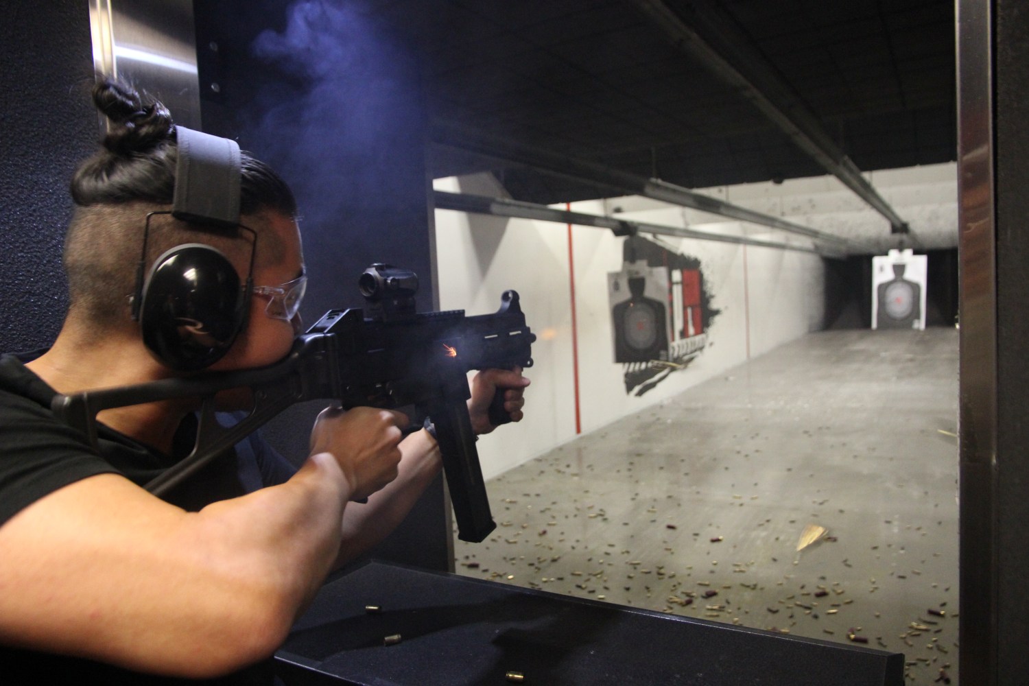 Person wearing ear protection fires a gun at an indoor shooting range.