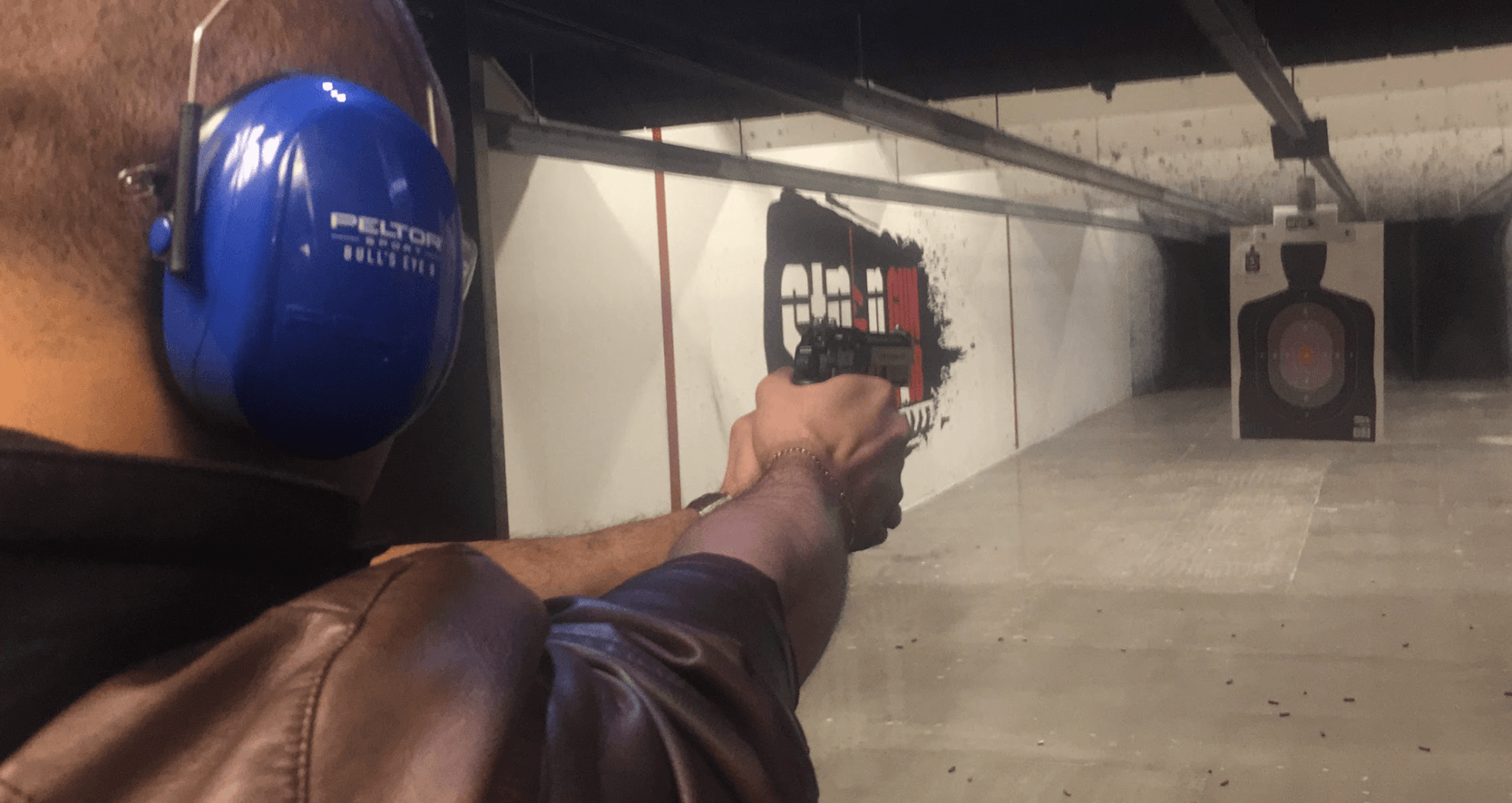 Shooter firing a semi-automatic pistol at an indoor target at Strip Gun Club's shooting range, illustrating the hands-on experience of comparing handgun calibers.