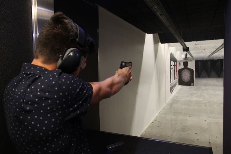 Person aiming a handgun at a target in an indoor shooting range.